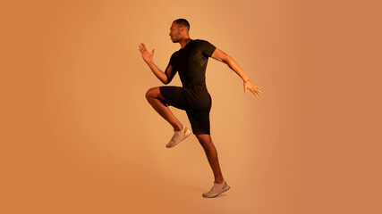 Fototapeta na wymiar Motivated african american sportsman running wearing black sportswear, brown background