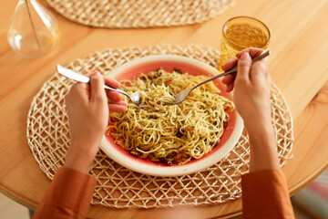 Lady eating tasty Italian pasta with parmesan cheese, holding fork and spoon, spaghetti wind it...
