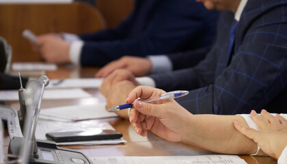 Woman, sitting at a table with men, during a meeting or negotiations, holds a pen and studies paper...