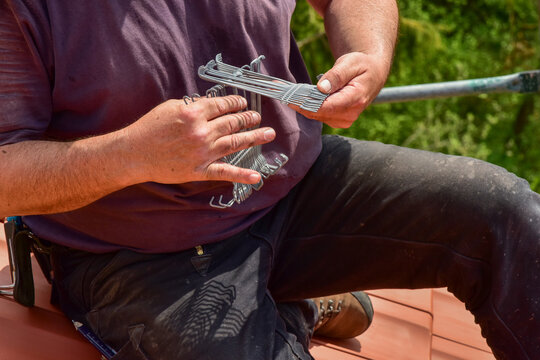 Der Dachdecker verwendet Seitenfalzklammern oder Sturmklammern, um die &auml;u&szlig;eren Ziegelreihen des Dachs gegen Sturmschaden zu sichern