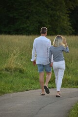 young slender man and woman are walking along the road near the fields