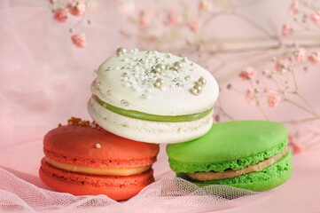 Obraz na płótnie Canvas Colored macaroons with decor close-up on a pink blurred background with flowers. Selective focus, natural light