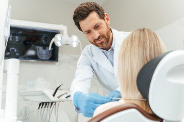 Obraz premium Portrait of handsome middle aged dentist consulting female patient with blond hair, in dental chair