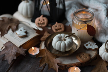 Autumn home composition with aromatic candle, pumpkin, wool sweater, halloween homemade cookies. Aromatherapy on a grey fall morning, atmosphere of cosiness and relax. Holiday handmade decor
