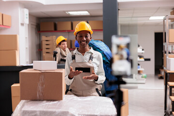 Woman taking smartphone video with customer order packing in retail storehouse. Smiling ecommerce shop warehouse worker looking at mobile phone camera and showing parcel preparation for dispatching