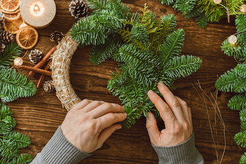 Top view of male hands making a Christmas wreath from natural spruce branches and various decorations