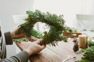 A man makes a Christmas wreath at home from natural materials. Ecological lifestyle. Do-it-yourself...