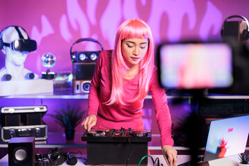 Smiling woman mixing techno music at professional mixer console having fun while performing song at...