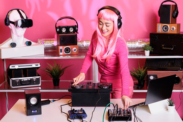 Musical artist with pink hair playing techno song at professional mixer console, enjoying...