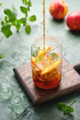 Summer cold drink, iced tea with nectarine or peach, ice and mint in a glass beaker on a green concrete background. Soft drinks, cold tea.