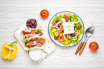Traditional Greek Food: Greek Salad, Gyros with meat and vegetables, Tzatziki sauce, Olives on White rustic wooden table background top view. Cuisine of Greece