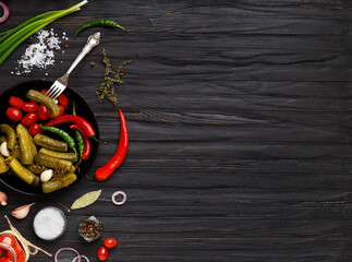 Assorted pickled vegetables in a black plate on a dark background, top view, copy space