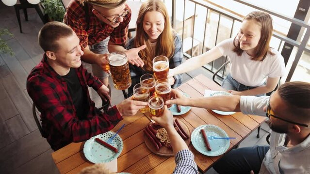 Top view of cheerful young people, friends meeting at cafe, pub, spending time together, drinking beer with sausages and snacks. Concept pktoberfest, traditional taste, friendship, leisure time, joy