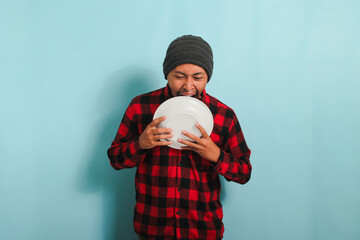 Funny, hungry Young Asian man with a beanie hat and a red plaid flannel shirt is pretending to bite...