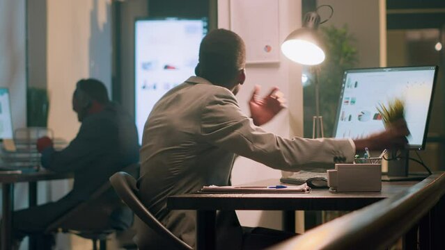 African american employee pissed about noisy coworker listening to music and pretending to beat drums in office. Businessman frustrated with overzealous colleague banging desk