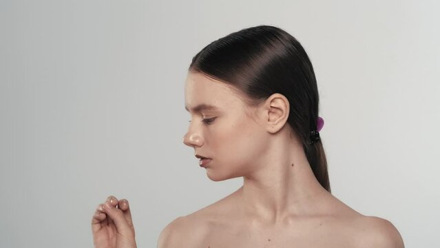 Brunette young model looking at her hand and nails, feather falling beahind. Slow motion