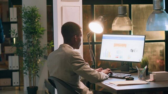 Meticulous accountant imputing revenue figures on computer in office during nightshift. Adept employee at desk focused on typing company statistical numbers, working overnight