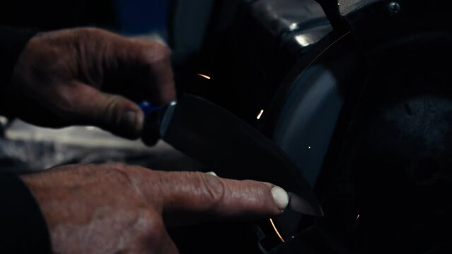 Men's hands work at a machine. Sparks fly from the hot metal. Man worked hard on steel. Machine sharpening on an electric grinder, manual sharpening on a rotary grinding stone, close-up.