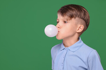Boy blowing bubble gum on green background, space for text