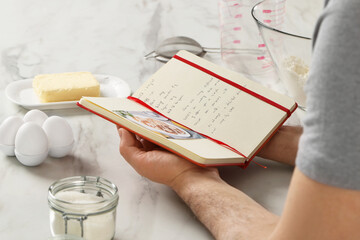 Man with recipe book at white marble table in kitchen, closeup