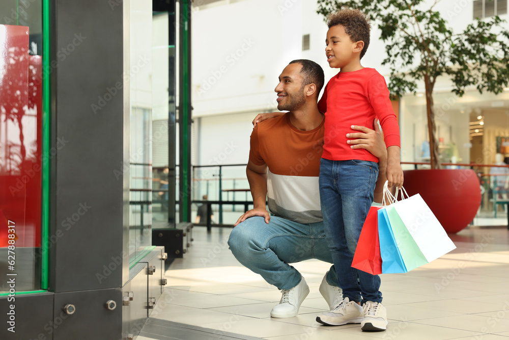 Wall mural Family shopping. Happy father and son with colorful bags in mall