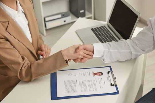 Human resources manager shaking hands with applicant during job interview in office, closeup