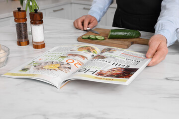 Man reading recipe in culinary magazine while cooking at home, closeup