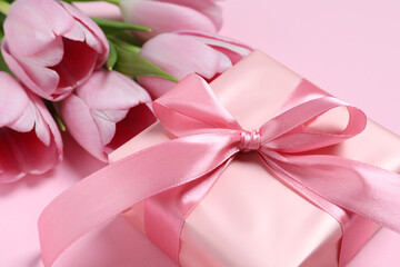 Beautiful gift box with bow and tulips on pink background, closeup