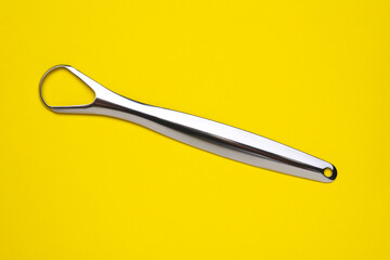 Metal tongue cleaner on yellow background, top view