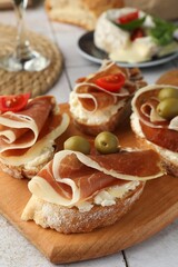 Tasty sandwiches with cured ham, tomatoes and olives on table, closeup