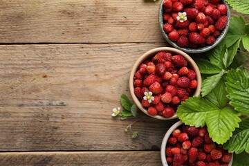 Fresh wild strawberries in bowls and leaves on wooden table, flat lay. Space for text