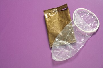 Unrolled female condom and torn package on violet background, above view with space for text. Safe...