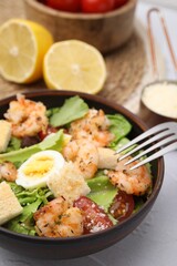 Delicious Caesar salad with shrimps and fork served on white table