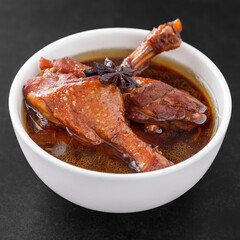 brown Chinese stewed calf of duck leg with Chinese Star Anise herb on top in white bowl on dark tone texture background, Thai food, Ped Pa Lo, Ped Palo, Ped Palow