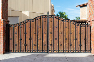 Two large elegant black metal closed gates with ornate details and brown wooden backing. The iron...