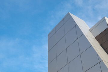 The exterior wall of a contemporary commercial style building with aluminum metal composite panels in various shapes. The futuristic building has engineered diagonal cladding steel frame panels. 