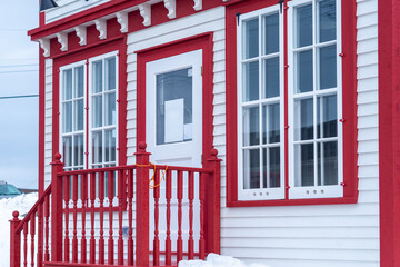 The exterior of a vintage convenience store with multiple large glass windows, a white wooden door...