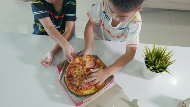 Happy Asian two little boy 5 years sitting eating huge pizza together on table at home, children eating unhealthy food, Excited funny kids eating pizza, Preschool mealtime with friends