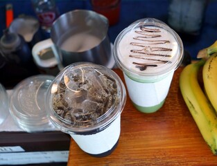 A top veiw of a cool beverage  in plastic cups with a bananas on a wooden table in the cafe to preparing to customer.
