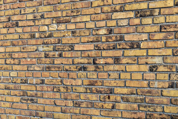 Full frame texture background of a shabby chic old mottled yellow and brown color exterior brick wall, with weathered bricks in a common bond brickwork pattern (angle view)