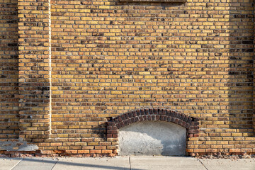 Full frame texture background of a shabby chic old mottled yellow and brown color exterior brick wall, with view of an enclosed arched basement window