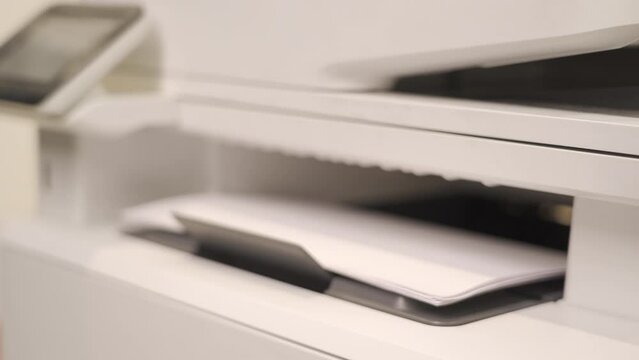 The office printer is working, white sheets come out of the printer, close-up