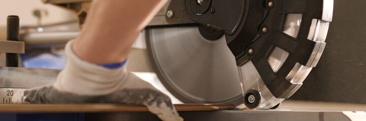 Construction worker sawing wooden board with power end saw closeup