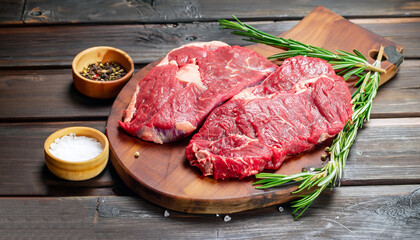 Raw meat. Raw beef steak on a cutting board with rosemary and spices.