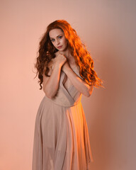 Close up portrait of beautiful brunette  female model wearing a cream dress with golden back light lighting.
Gestural arm poses with hands reaching out, isolated on studio background.
