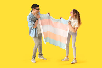 Young couple with transgender flag on yellow background