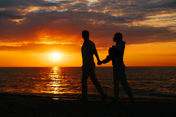 Romance, sunset date. Silhouette of guy and girlfriend holding hands together walking along shore by sea, young couple in love