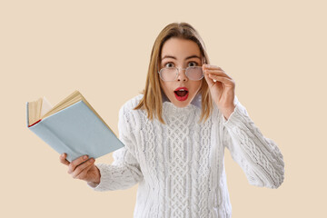Shocked young woman with book on beige background