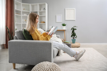 Young woman reading book on sofa at home