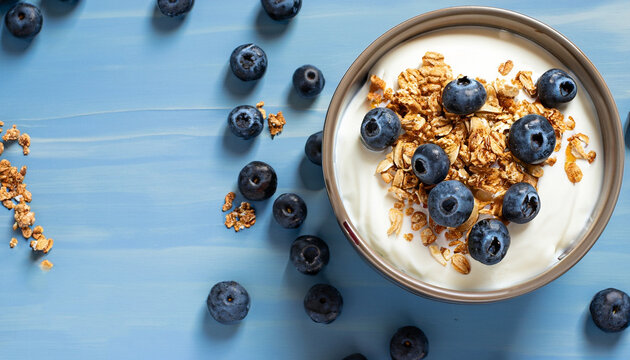 Greek yogurt granola and blueberries on blue table top view. Healthy food nutrition, snack or breakfast.